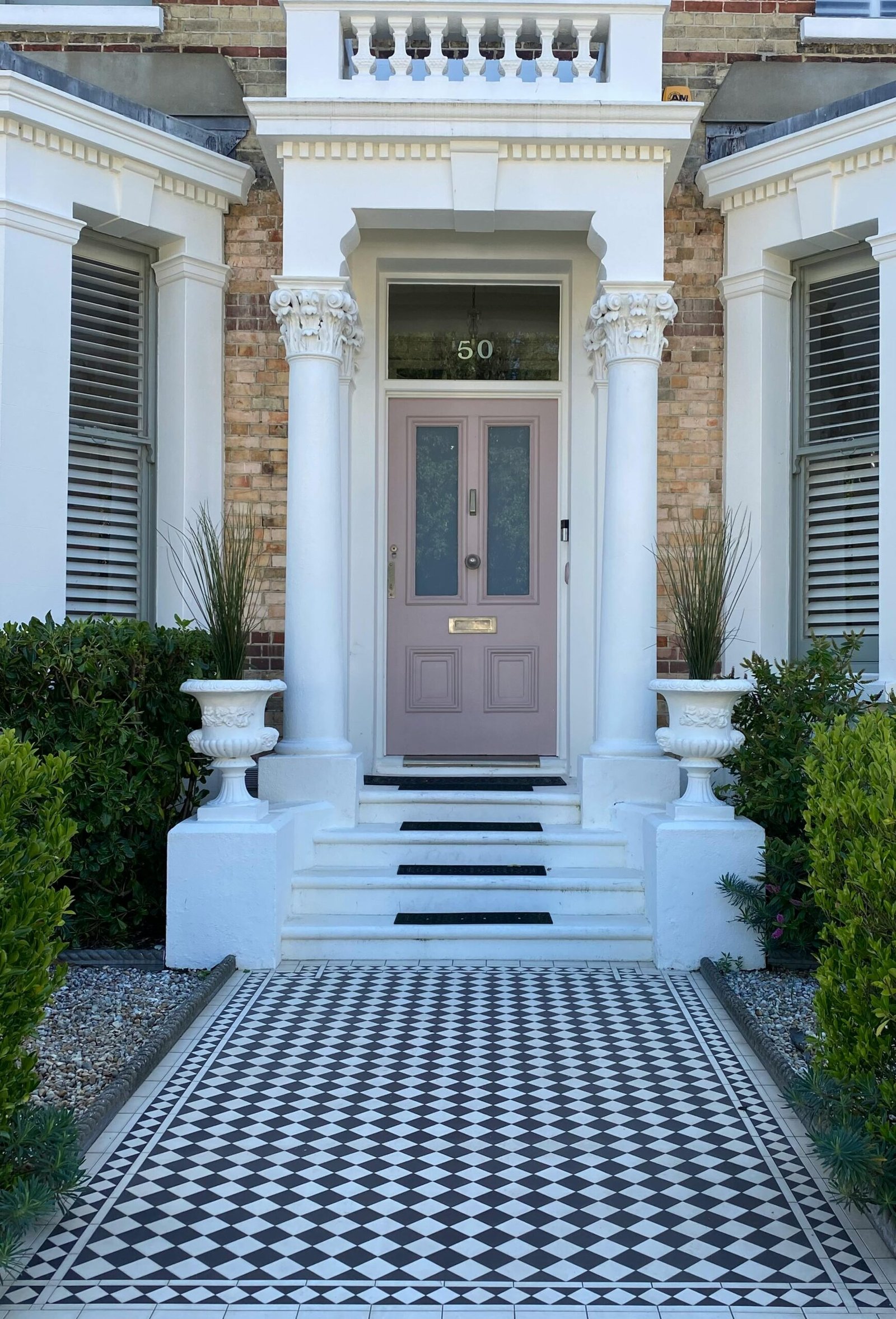 Beautiful Victorian house entrance featuring columns and black and white tile pathway.